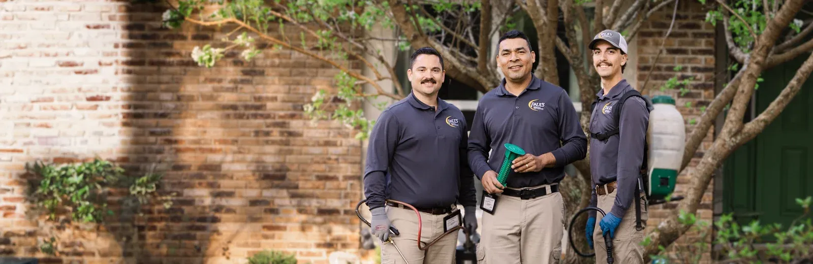 Paul's Pest Control Technicians standing in front of brick home